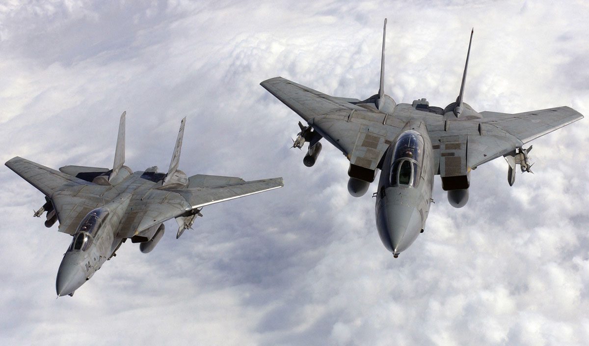 Two jets flying in the sky with clouds behind them.