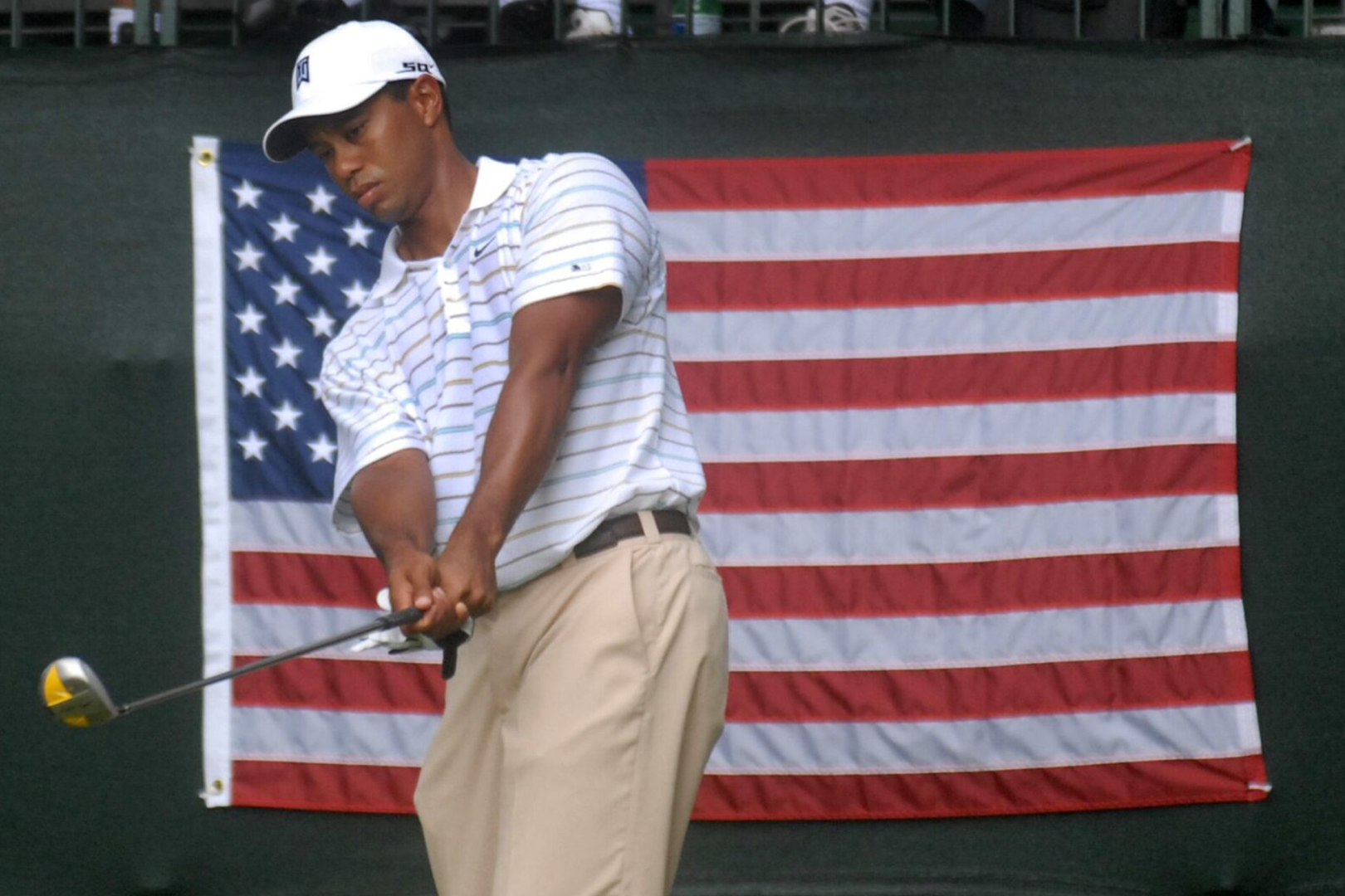 A man holding a golf club in front of an american flag.