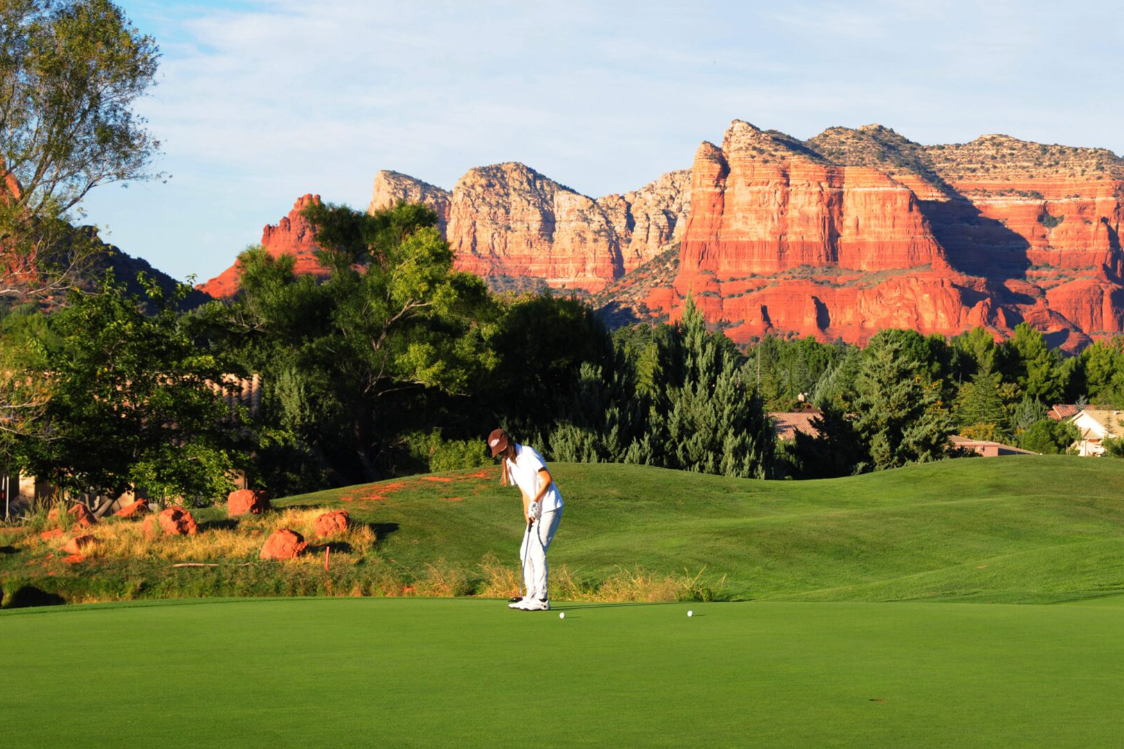 A man playing golf on the green with mountains in the background.